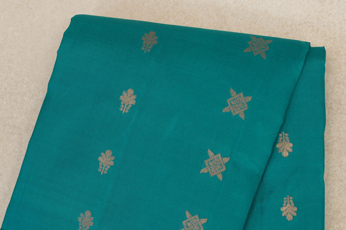 Folded close-up of a peacock green Kanchipuram silk saree body with spaced gold-colored floral and star-shaped motifs.