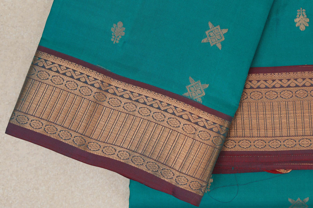Folded peacock green Kanchipuram silk saree with small gold-toned motifs and a broad patterned border edged in maroon.