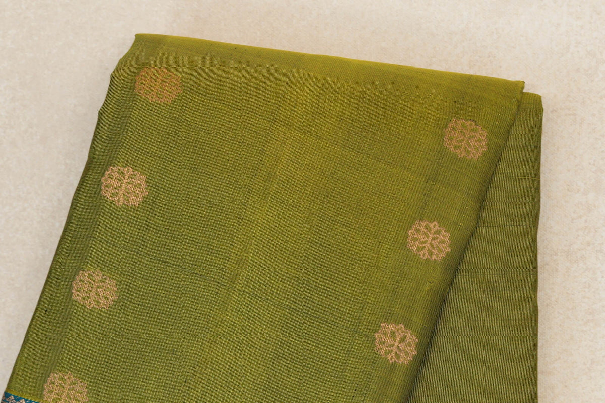 Folded olive green lightweight Kanchipuram silk saree with spaced gold-toned floral motifs and a glimpse of its teal blue border.